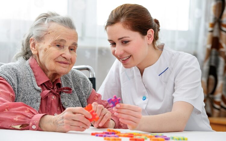 Elder care nurse playing jigsaw puzzle with senior woman in nursing home