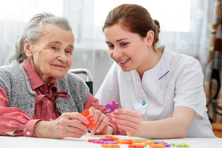 Elder care nurse playing jigsaw puzzle with senior woman in nursing home